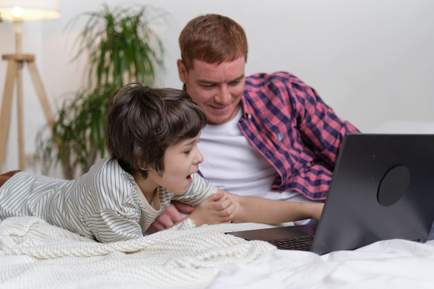 楽しい子供がパパの注目を集めながらラップトップとシリーズでリラックスしようとしています