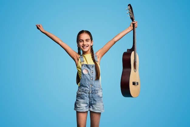 Photo joyful child with acoustic guitar raising arms after successful performance