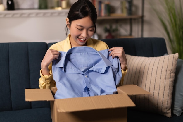 즐거운 중국 여자 집에서 파란색 셔츠를 들고 상자 풀기