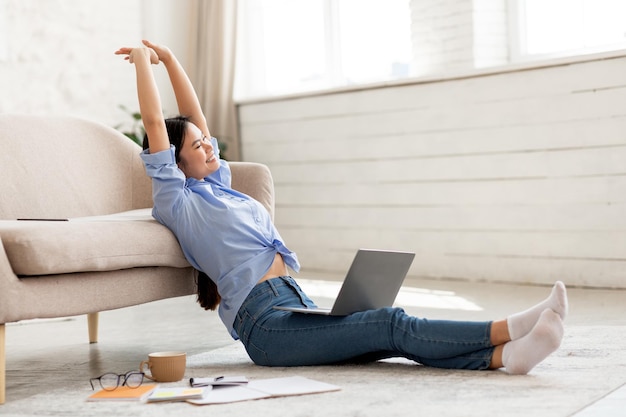 Joyful chinese woman stretching while using laptop