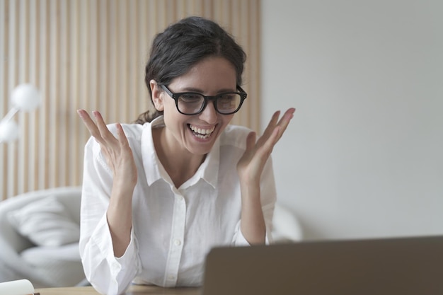 うれしそうなコーチイタリアの女性は、オンラインで学生と通信しながらノートパソコンの画面を見ます