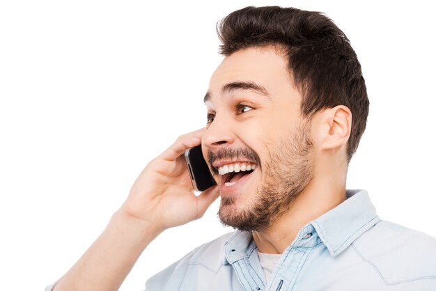 Joyful communication. Portrait of cheerful young man talking on the mobile phone and smiling while standing against white background