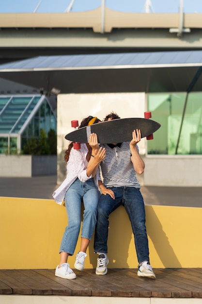 Joyful couple kiss hiding above longboard playful man and woman in love together hold skateboard