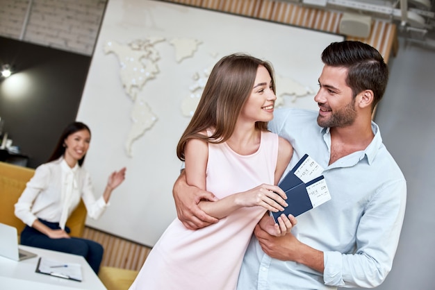 Joyful couple looking to each other and holding passport with flying tickets