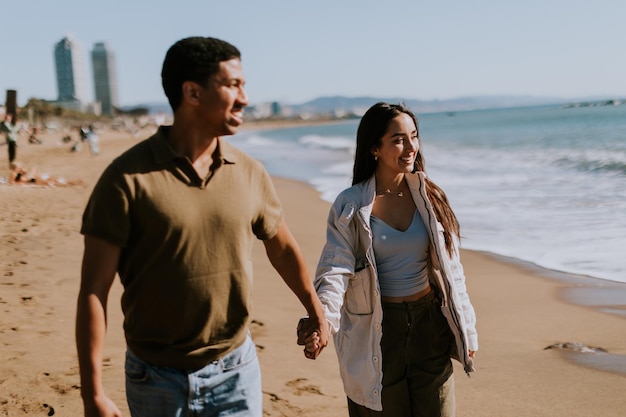 Photo joyful couple running hand in hand along a sunlit beach in barcelona spain