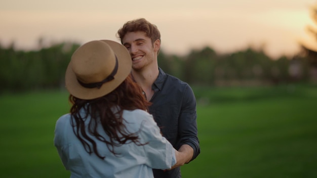 Joyful couple turning around on green field in slow motion Loving man and woman jumping on meadow in summer park Happy people spending time together at romantic date at sunset