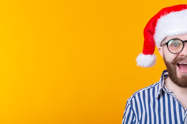 Joyful crazy cute young hipster male in red santa claus hat posing over yellow wall. the concept of christmas