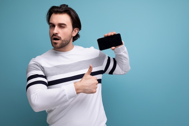 Joyful cute young guy with black hair points finger at advertising