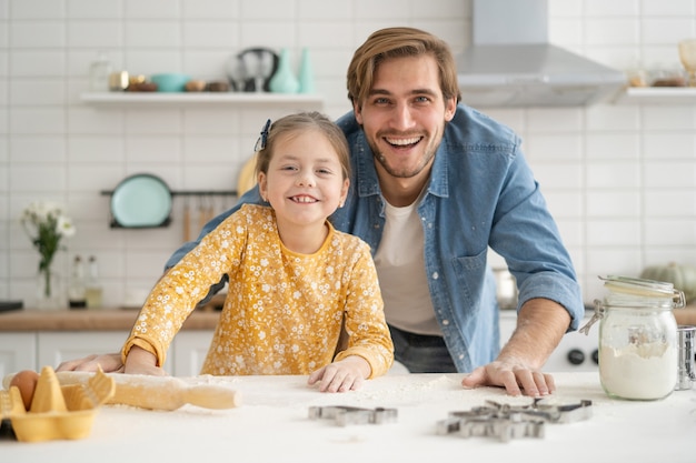 Joyful dad and daughter having fun while kneading dough on kitchen table, baking together. Family cooking concept