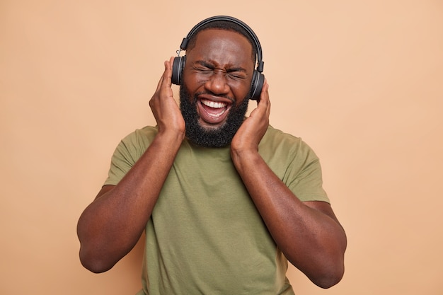Joyful dark skinned man has fun enjoys favorite music wears wireless headphones