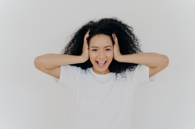 Joyful dark skinned woman keeps hands on head