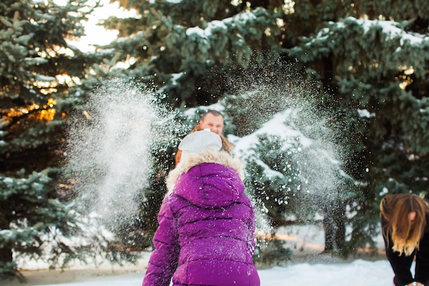 Joyful daughter throwing snowball at parents in winter park Happy winter holidays