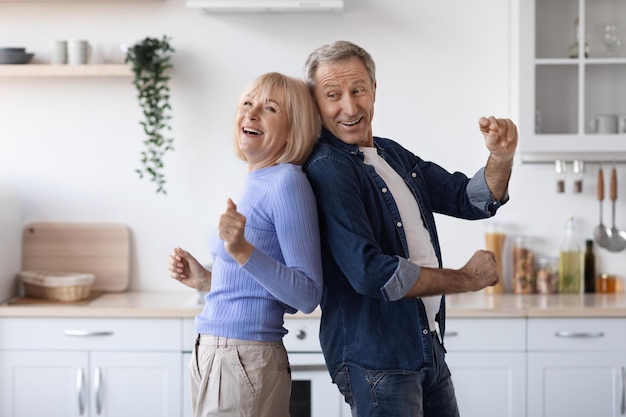 Joyful elderly spouses dancing together at kitchen