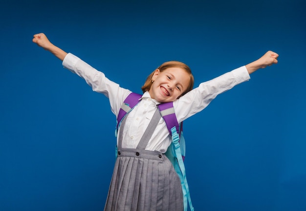 A joyful excited teenage girl clenching her fists is genuinely happy and laughing loudly on a blue background A pretty schoolgirl is smiling The concept of children's happiness