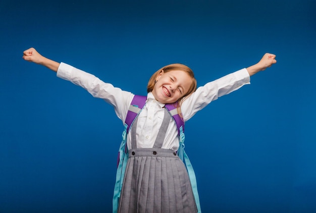 A joyful excited teenage girl clenching her fists is genuinely happy and laughing loudly on a blue background A pretty schoolgirl is smiling The concept of children's happiness