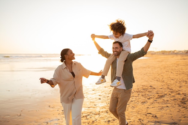 楽しい家族のビーチの日楽しんでいる幸せな家族 父親が息子を肩に担いで歩いている