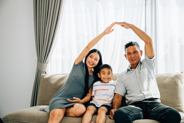 Photo a joyful family poses on a sofa parents making a roof gesture above their little son