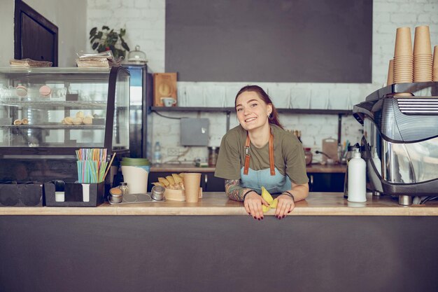 カフェのカウンターの後ろに立っているうれしそうな女性バリスタ