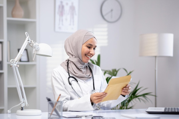 Joyful female doctor in hijab received envelope message mail notification with good results of