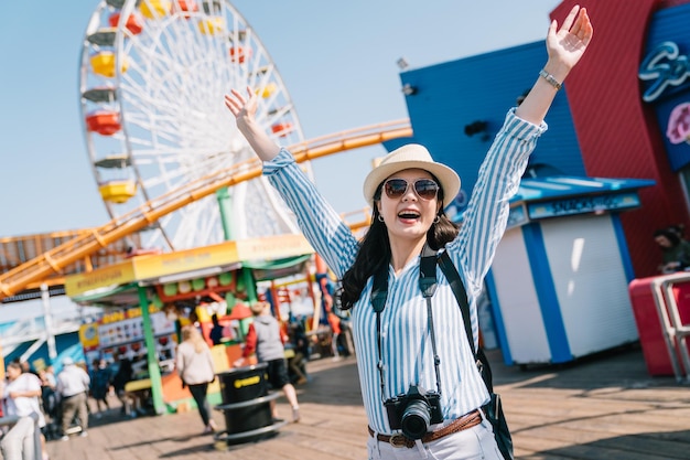 a joyful female traveler excited raising her arms to the sky, face to camera smiling