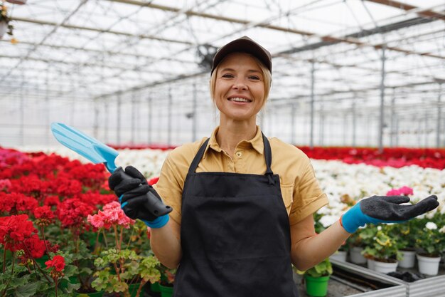 手にこてを持った花の温室のうれしそうな女性労働者