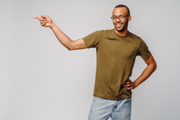 Joyful friendly african-american young man in green t-shirt pointing by finger at blank space