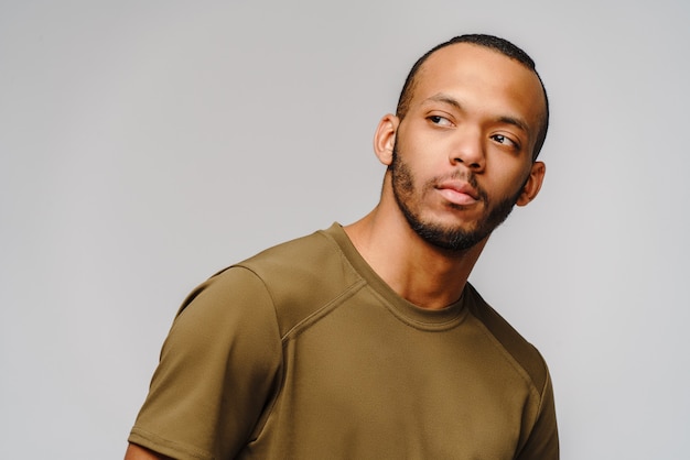 Joyful friendly young man in a green t-shirt over light grey background