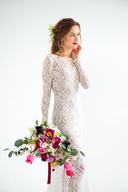 Joyful girl bride in a white knitted dress posing with a bouquet of flowers