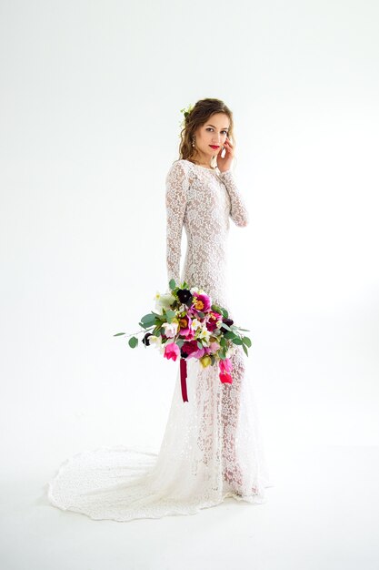 Joyful girl bride in a white knitted dress posing with a bouquet of flowers