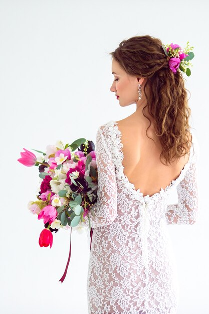 Joyful girl bride in a white knitted dress posing with a bouquet of flowers