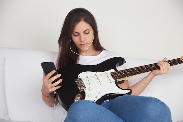 Joyful girl in earphones watching electric guitar tutorial on
mobile phone