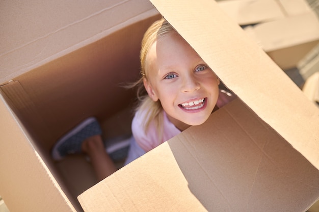 Joyful girl hiding in big box on street