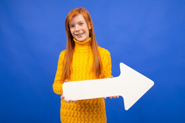 Joyful girl holding a white arrow pointer to the right on blue