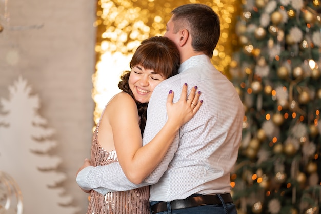 Una ragazza allegra abbraccia un ragazzo tra scintillii e ghirlande a una festa di natale