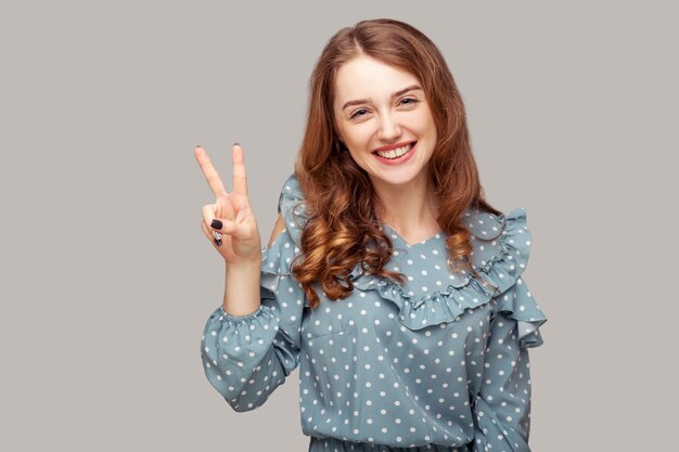 Ragazza gioiosa che mostra la pace della vittoria guardando la telecamera con un sorriso a trentadue denti che si gode la vittoria della vittoria