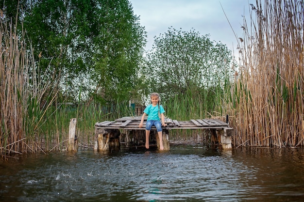 Joyful girl splashing with legs in water on the pier at lakeshore happy childhood