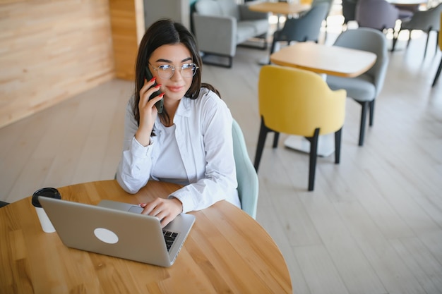 Joyful girl student studying online at cafe using laptop and earphones empty space