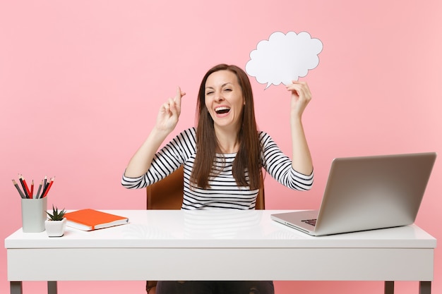 Joyful girl wait for special moment keeping fingers crossed hold empty blank Say cloud speech bubble work at office with pc laptop