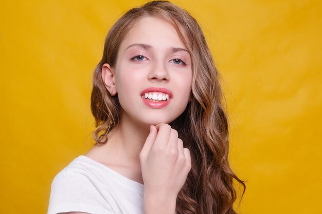 Joyful girl with beautiful brunette hair on yellow background. Kid's style. Hairstyle. snow- white smile, large locals of hair