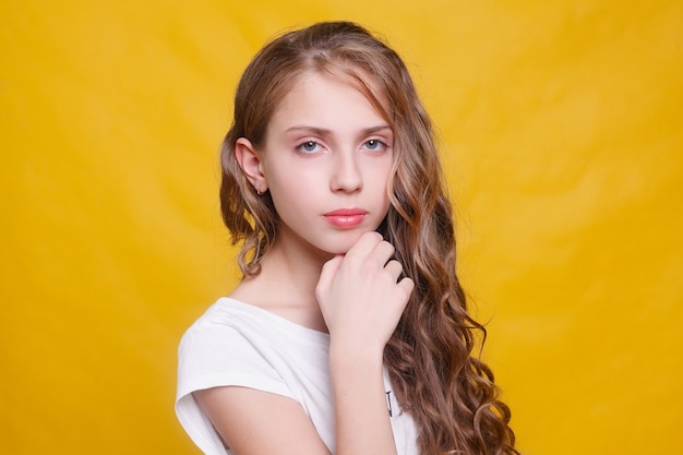 Joyful girl with beautiful brunette hair on yellow background. Kid's style. Hairstyle. snow- white smile, large locals of hair