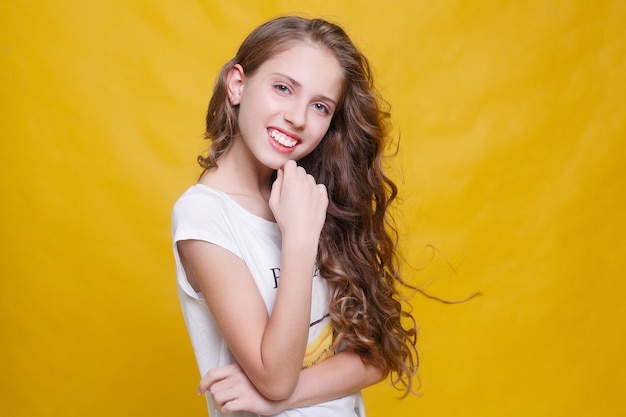 Joyful girl with beautiful brunette hair on yellow background. Kid's style. Hairstyle. snow- white smile, large locals of hair