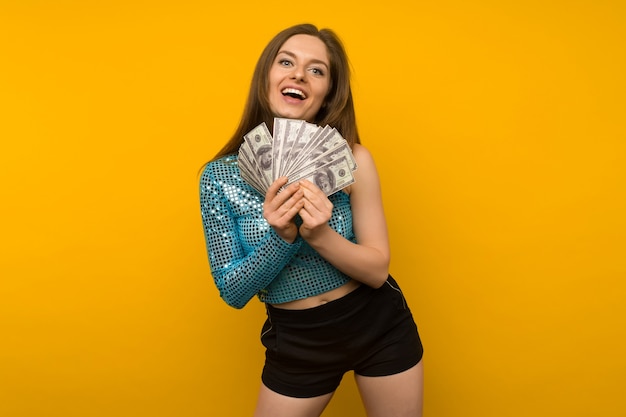 Joyful girl won the lottery and holds a fan of us dollars in her hands on a yellow background