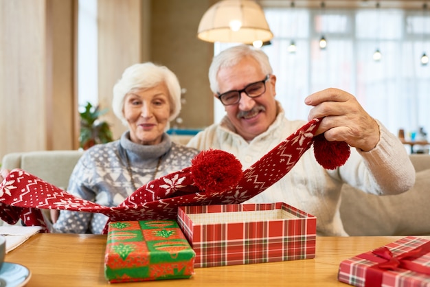Радостные бабушка и дедушка открывают рождественские подарки за столом
