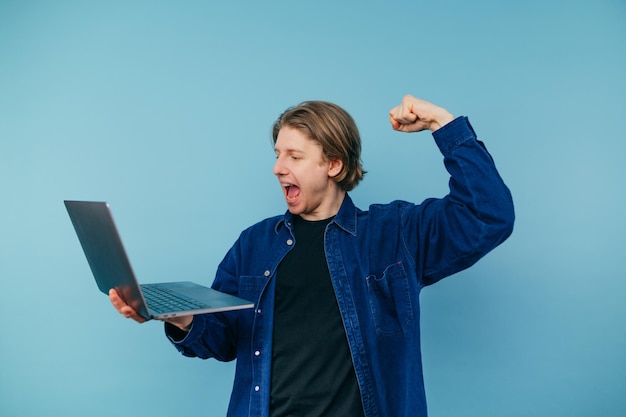 Joyful guy in a shirt with a laptop in hand emotionally rejoices looking at the screen screams