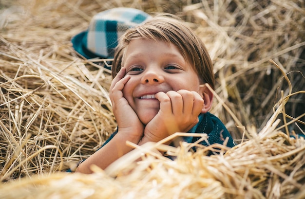 Joyful guy with a hat on his head in the hay the boy advertises childrens clothes for the autumn