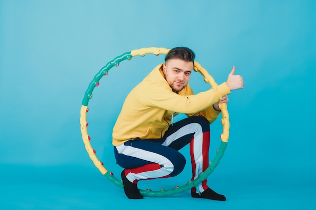 joyful guy in a yellow blouse with a hula hoop shows a liking on a blue background