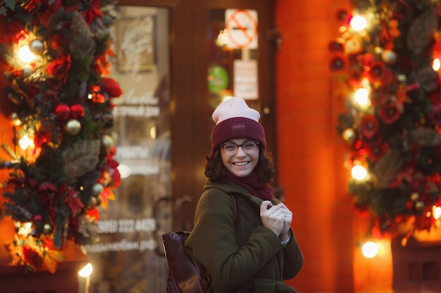 Gioiosa ragazza felice godendo del tempo nevoso sulla strada sorridere e godersi la vita indossa un elegante cappotto di pelliccia cappello lavorato a maglia e ampia sciarpa atmosfera festiva atmosfera natalizia vera felicità