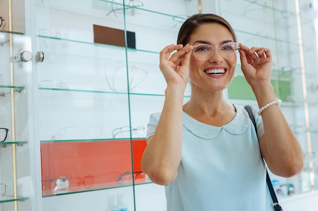 Joyful happy woman smiling while trying stylish eyeglasses on