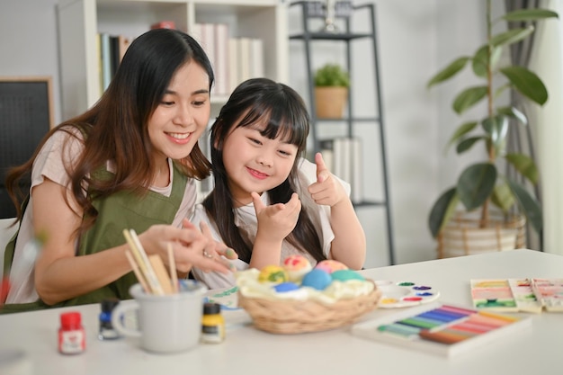 Joyful and happy young Asian girl enjoys making Easter eggs with her sister in the kitchen