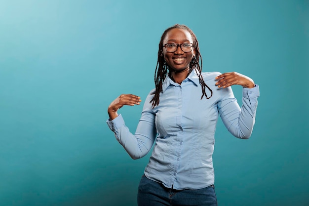 Joyful happy young woman dancing with pleasure while listening to music playlist. Cheerful pleased adult person vibing through dance while celebrating an important event. Studio shot.